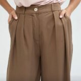 Pantalones de mujer en color marrón con pinzas y botón en la parte frontal, combinados con una blusa rosa, ideales para un look casual y elegante.