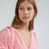 Mujer con blusa de cuadros rosas y tirantes a rayas, mirando hacia un lado, fondo neutro.