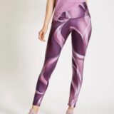Mujer usando leggings de diseño abstracto en tonos morados y rosas, combinados con una camiseta rosa y zapatillas deportivas gris claro, ideales para actividades deportivas y casuales.