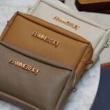 Tres bolsos de mano en tonos neutros (beige, marrón claro y marrón oscuro) con detalles dorados, dispuestos sobre una mesa de mármol. Ideal para accesorios de moda.