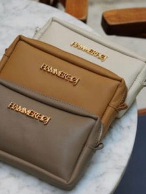 Tres bolsos de mano en tonos neutros (beige, marrón claro y marrón oscuro) con detalles dorados, dispuestos sobre una mesa de mármol. Ideal para accesorios de moda.