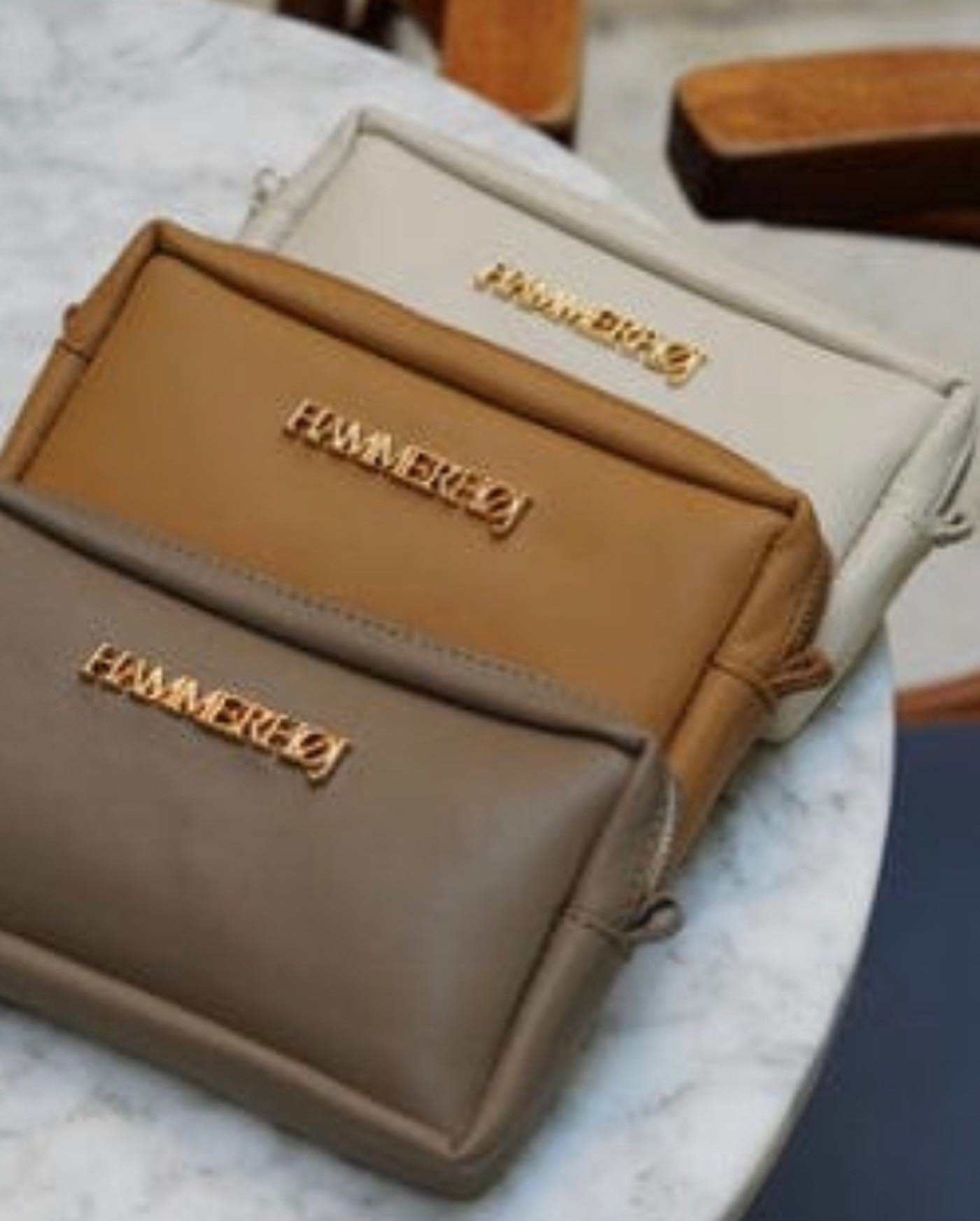 452995706_18362567638098092_4191653010420226657_n Tres bolsos de mano en tonos neutros (beige, marrón claro y marrón oscuro) con detalles dorados, dispuestos sobre una mesa de mármol. Ideal para accesorios de moda.