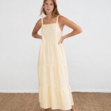 Mujer joven posando con un vestido largo amarillo de tirantes en un fondo blanco, destacando un estilo fresco y veraniego. Ideal para ocasiones casuales.
