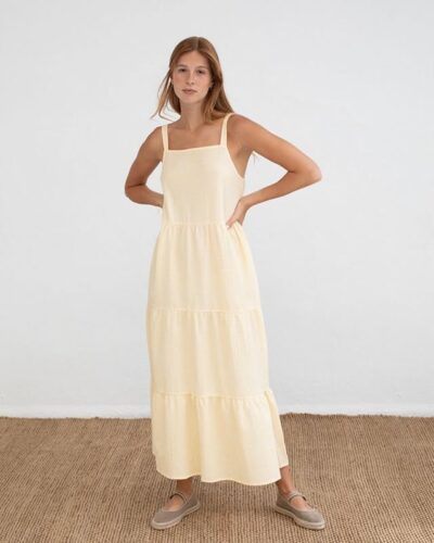 Mujer joven posando con un vestido largo amarillo de tirantes en un fondo blanco, destacando un estilo fresco y veraniego. Ideal para ocasiones casuales.