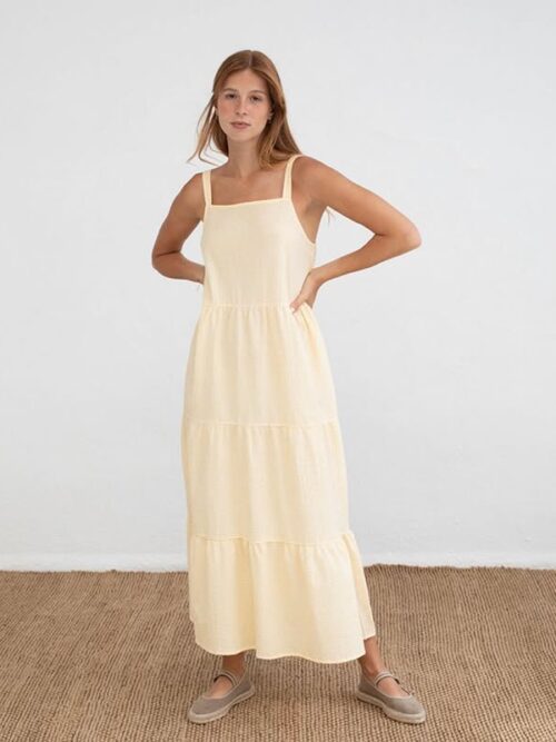 Mujer joven posando con un vestido largo amarillo de tirantes en un fondo blanco, destacando un estilo fresco y veraniego. Ideal para ocasiones casuales.