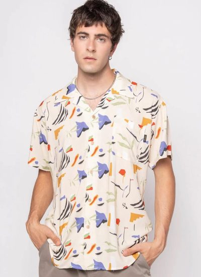 Hombre joven posando con una camisa de estampado abstracto en tonos beige, azul, naranja y verde, luciendo un estilo moderno y casual.