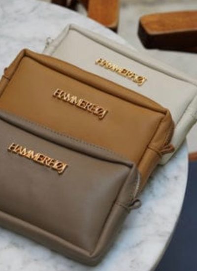 Tres bolsos de mano en tonos neutros (beige, marrón claro y marrón oscuro) con detalles dorados, dispuestos sobre una mesa de mármol. Ideal para accesorios de moda.